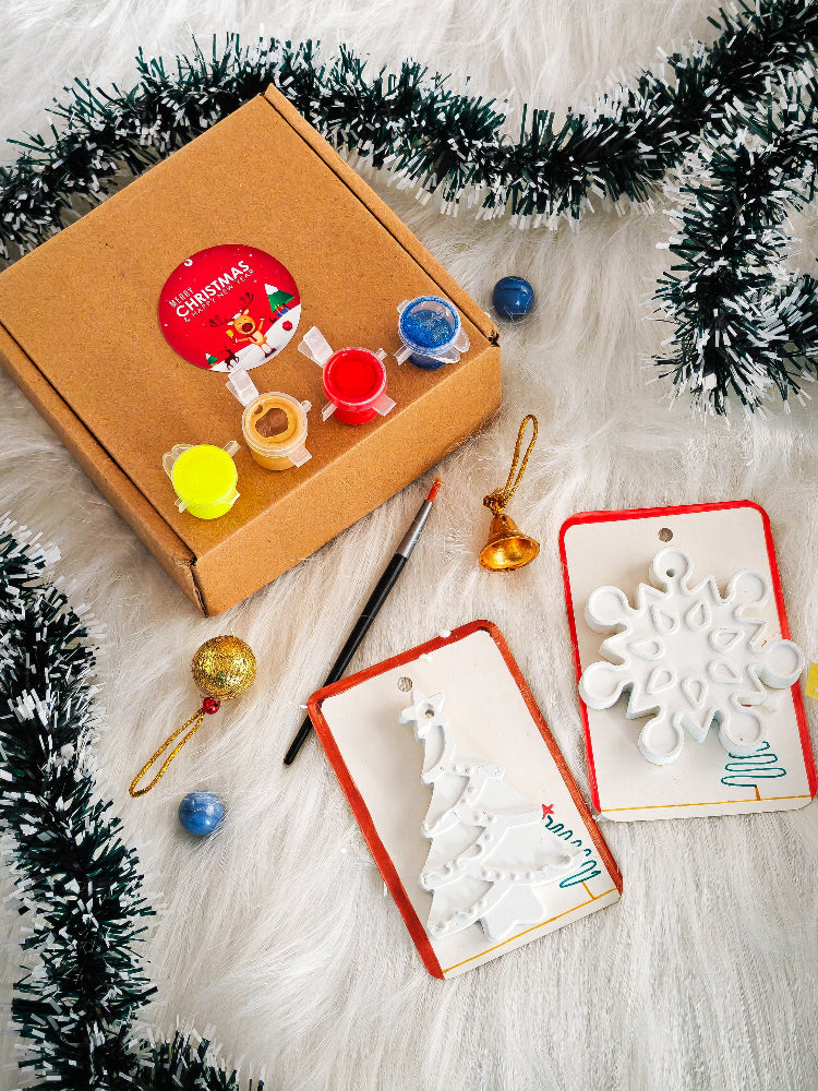 Crafting kit with paint, brushes, and decorative items on a textured surface with tinsel.