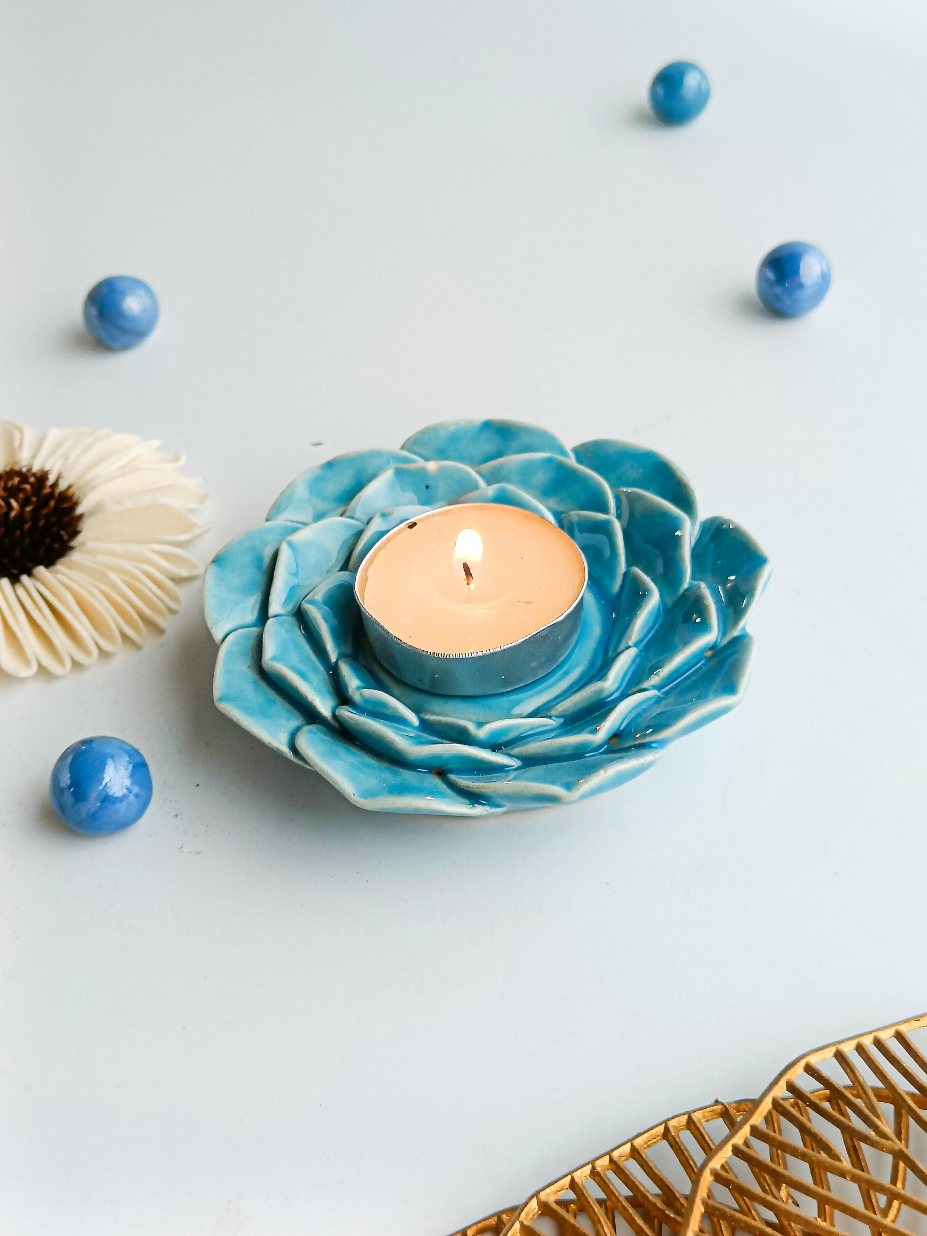 Blue flower-shaped candle holder with a lit candle on a light gray background