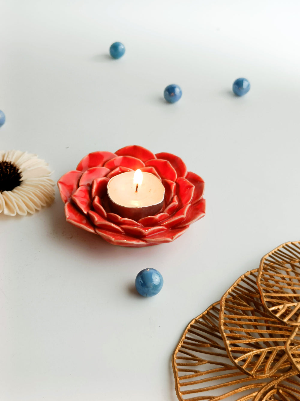 Red flower-shaped candle holder with a lit candle on a light gray background